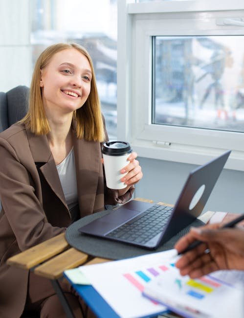 Smiling woman enjoys coffee while working on laptop in modern office.
